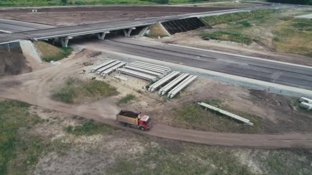 Far volare un elicottero su un camion che guida sulla strada. Costruzione di un incrocio stradale. Colonna di polvere da un camion di passaggio. Industrializzazione, sviluppo urbano. Costruzione di una nuova strada. — Video Stock