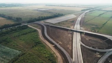 Trafik kavşağının üzerinden uçun. Otoyol kavşağı. Yol yapım aşamasında. Güzel manzara. Tarlalar ve ormanlar arasında otoyolun manzaralı bir manzarası. Ülke parçası