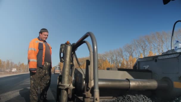 Novoszibirszk régió, 2020. augusztus 3. Novoszibirszk közúti szállítás. Férfiak a munkahelyen. Aszfaltozott út. Egy overálos munkás irányítja az aszfaltkeverék öntésének folyamatát. Porlasztott aszfaltburkolat — Stock videók