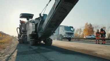 Novosibirsk bölgesi, 3 Ağustos 2020. Yol yüzeyi tamiri. Asfalt yolu. Öğütücü ve öğütücü gün batımında. Tulumlu işçiler konuşuyor. Yol inşa makineleri.