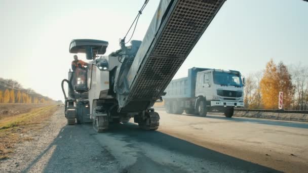 Novosibirsk, 3 augustus 2020. Een wegenwerker gebruikt bij zonsondergang een frees- en slijpmachine. Reparatie van wegdek. Asfaltweg. Wegenbouwmachines. — Stockvideo