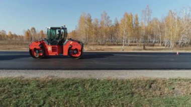Novosibirsk bölgesi, 3 Ağustos 2020. Yol yüzeyi tamiri. Yeni bir yol inşaatı. Dört silindirli yeni asfaltı sıkıştırıyor ve düzleştiriyor. Sonbahar ormanının arka planında yol silindirleri var. Bir katman