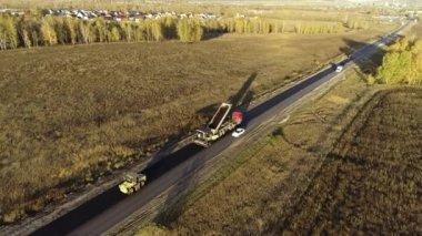 Hava görüntüsü. Yol tamiri. Asfalt karışımını kaldırıma yüklüyorum. Batan güneşin ışınlarında yeni bırakılmış asfalt. Ormanlar ve tarlalar arasında karayolunda yol çalışmaları.