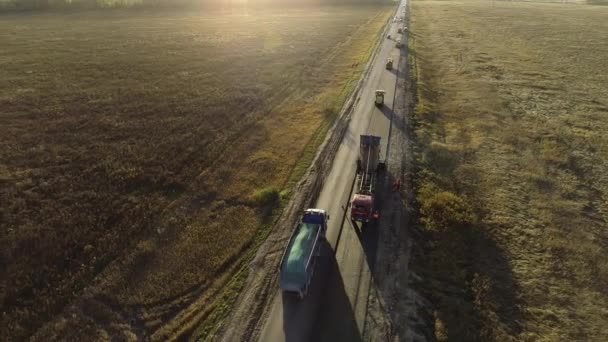 Volo dell'elicottero attorno all'attrezzatura per la costruzione di strade. Riparazione stradale. Caricamento della miscela di asfalto nel paver. Asfalto appena posato nei raggi del sole al tramonto. Uomini al lavoro. Riverbero del sole. — Video Stock