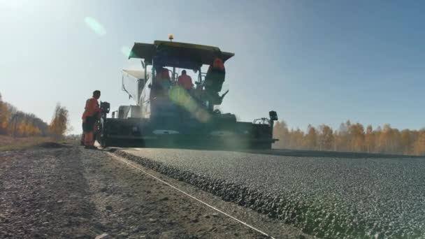 Novosibirsk, 3 de agosto de 2020. Construcción de una nueva carretera. Reparación. Los trabajadores con overoles están trabajando con una pavimentadora de asfalto. Una capa de asfalto recién puesto al atardecer. Vapor de asfalto caliente — Vídeo de stock