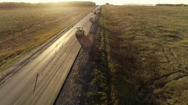 秋天风景中道路上的工程的空中视图.压路机把沥青压平,铺路机把沥青压平.道路建筑机械。美丽的日落. — 图库视频影像