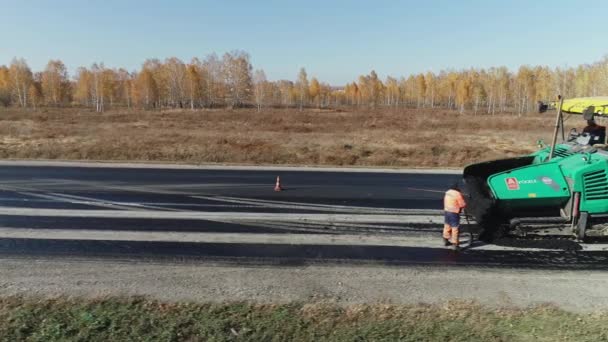 Útfelület javítás. Egy új út építése. Az új aszfaltburkoló aszfaltot rak. Útépítő járművek az őszi erdő hátterében. Egy réteg frissen fektetett aszfalt. — Stock videók