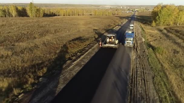 Veduta aerea di un camion che guida lungo un'autostrada in riparazione nei campi. Macchine per costruzioni stradali. Uno strato di asfalto appena deposto. Riparazione stradale. Paver asfalto, rulli stradali. — Video Stock