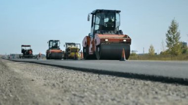 Yol silindirleri mavi gökyüzüne karşı asfaltı düzleştirir ve sıkıştırır. Yeni yerleştirilmiş bir asfalt tabakası. Yol yüzeyi tamiri. Yol tamiri. Yol yapım makineleri.