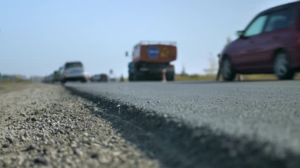 Profundidad de campo superficial. Primer plano de una carretera asfaltada recién pavimentada. Los coches pasan en la nueva superficie de la carretera fuera de foco. Reparación vial. — Vídeo de stock