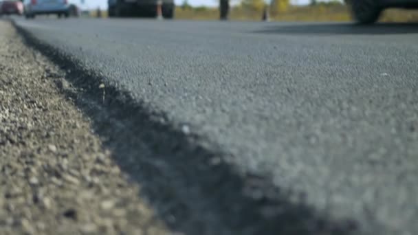 Ondiepe scherptediepte. Close-up van een pas aangelegde asfaltweg. Weg reparatie. Auto 's rijden buiten beeld op nieuwe snelweg. Zonnige dag. — Stockvideo