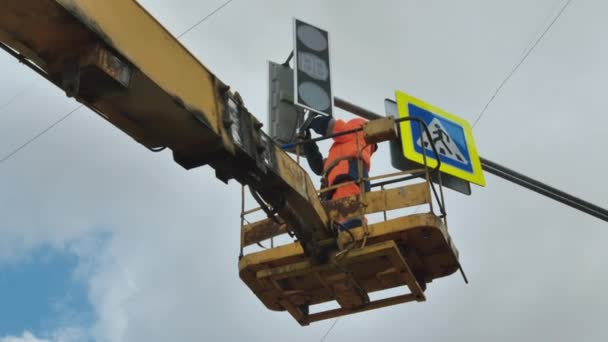 Een werknemer in een liftwieg repareert een LED-verkeerslicht tegen een achtergrond van wolken. Verkeerstekens. LED-technologie. Voetgangersoversteekplaats. — Stockvideo