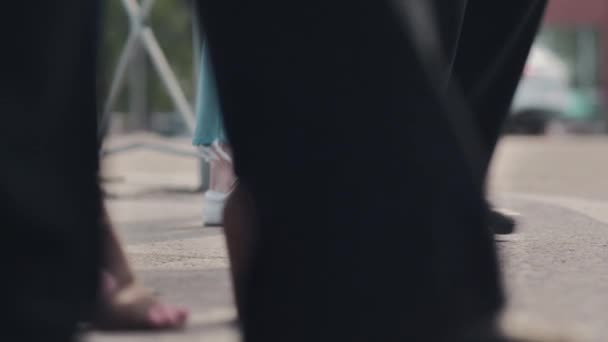 Uma multidão de pedestres atravessa a estrada contra o pano de fundo dos carros que passam. Crowded crosswalk durante a hora de ponta. Close-up de correr pernas de pessoas. Vida na cidade. Movimento lento — Vídeo de Stock