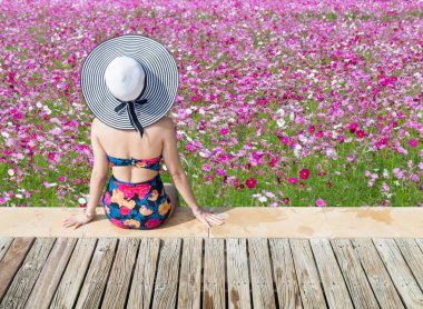Genç kadın bir ahşap iskele üzerinde pembe çiçekler üzerinde seyir mayo