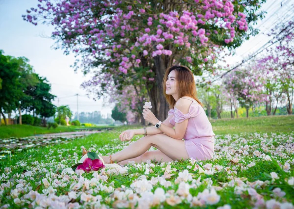 年轻的亚洲妇女坐在草地上与下降的樱花 — 图库照片