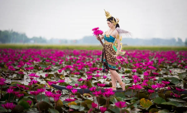 赤い蓮の花畑の池での木造船の上に立ってキンナリー服装の美しい女性は タイの伝統とタイのおとぎ話想像してイメージに従ってください — ストック写真