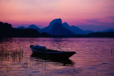 Barajdaki ahşap teknenin silueti, günbatımında gökyüzü alacakaranlığı.