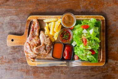 Kahverengi ahşap tabakta soslu ve sebzeli domuz pirzolası..