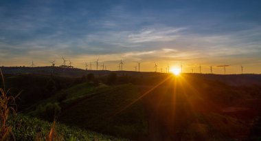 Siluet rüzgar türbini alacakaranlık gökyüzü ve güneş ışığı dağdaki temiz enerji santrali için..