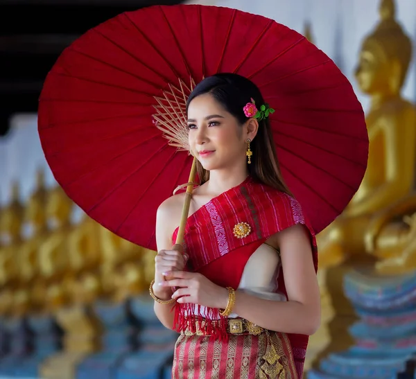 廊下を歩く赤い傘を持つ美しいタイの女性は タイのアユタヤ県の古代寺院でタイの伝統衣装を着た瞑想黄金の仏像を持っています — ストック写真