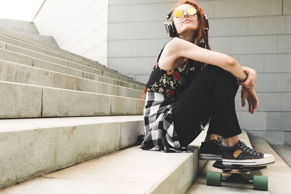 Junges Mädchen mit Tätowierung und Dreadlocks, das Musik hört, während es auf den Stufen sitzt — Stockfoto