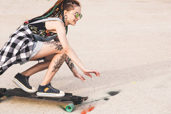 young girl with tattoo rides on a longboard