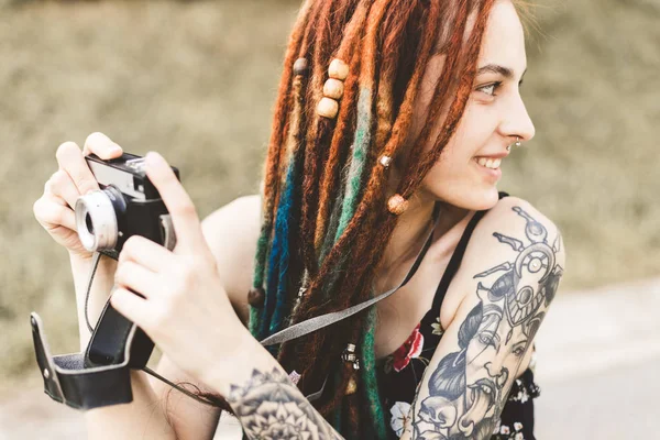 Chica joven con tatuajes y rastas fotografías cámara vintage en el parque —  Fotos de Stock