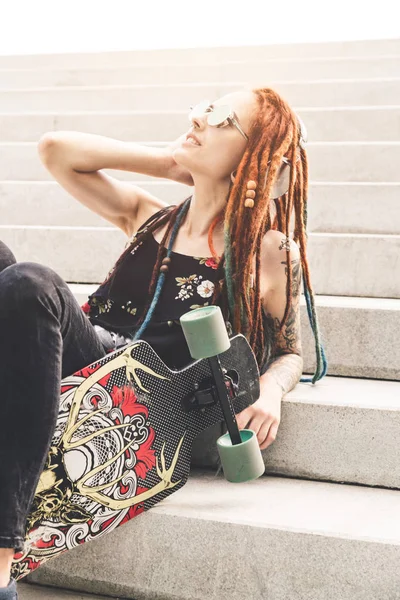 UFA, RUSIA - 12 de septiembre de 2018 Foto editorial de una joven con tatuaje y rastas escuchando música mientras está sentada en las escaleras — Foto de Stock