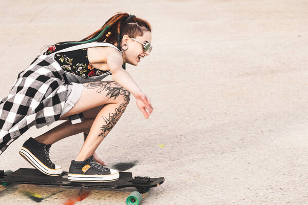 young girl with tattoo rides on a longboard