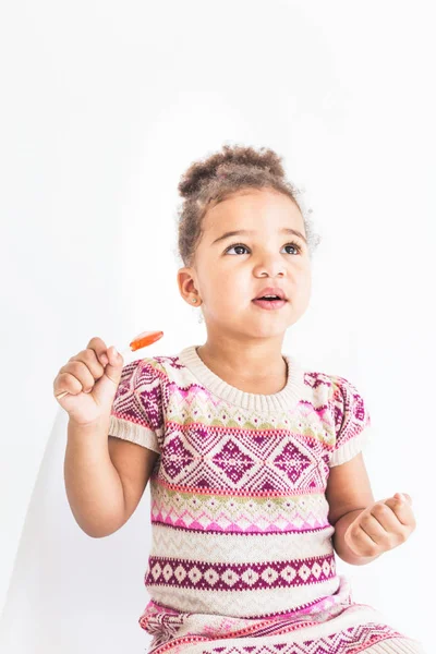 Retrato de una niña en un vestido colorido con una piruleta sobre un fondo blanco — Foto de Stock