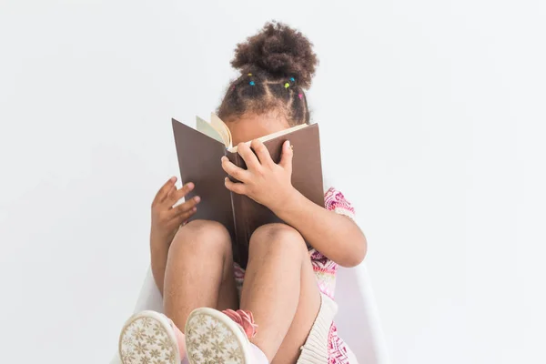 Retrato de una niña con un vestido colorido leyendo un libro sobre un fondo blanco — Foto de Stock