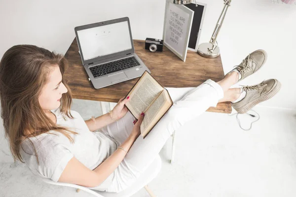 Joven mujer de negocios trabajando en casa y leyendo un libro con las piernas sobre la mesa. Espacio de trabajo de estilo escandinavo creativo. # Wiew from above — Foto de Stock