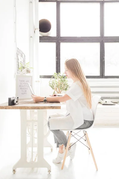 Νεαρή γυναίκα που εργάζονται στο σπίτι πίσω από ένα φορητό υπολογιστή. Δημιουργική σκανδιναβικό στυλ χώρου εργασίας — Φωτογραφία Αρχείου