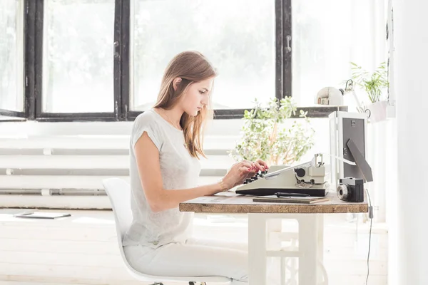 Νεαρή γυναίκα εργάζεται στο σπίτι και πληκτρολογώντας σε μια γραφομηχανή. Δημιουργική σκανδιναβικό στυλ χώρου εργασίας — Φωτογραφία Αρχείου