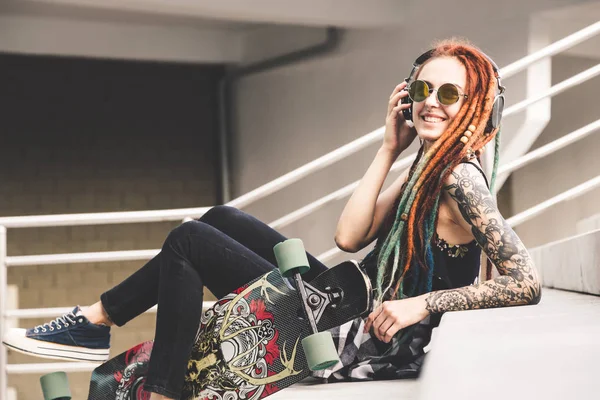 UFA, RUSIA - 12 de septiembre de 2018 Foto editorial de una joven con tatuaje y rastas escuchando música mientras está sentada en las escaleras —  Fotos de Stock