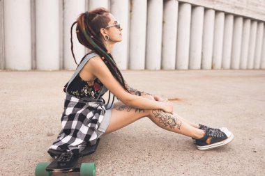 dövme ve dreadlocks bir longboard beton yapı zemin üzerine oturan genç kız