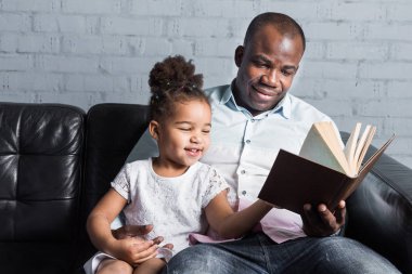 Ebeveynler kanepede oturan çocuklar için bir kitap okuyun. Mutlu çok ırklı bir aile. Aile değerleri