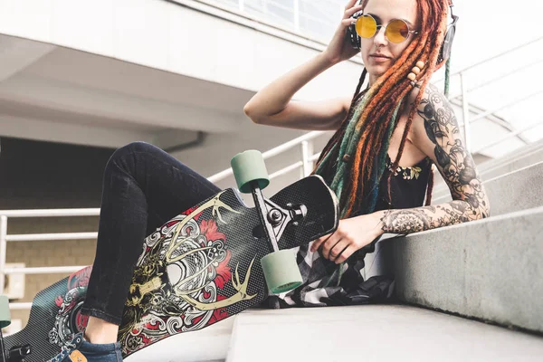 UFA, RUSIA - 12 de septiembre de 2018 Foto editorial de una joven con tatuaje y rastas escuchando música mientras está sentada en las escaleras —  Fotos de Stock