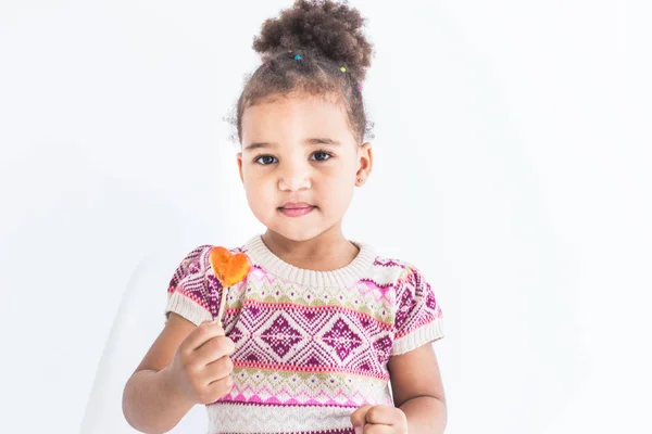 Retrato de una niña en un vestido colorido con una piruleta sobre un fondo blanco — Foto de Stock