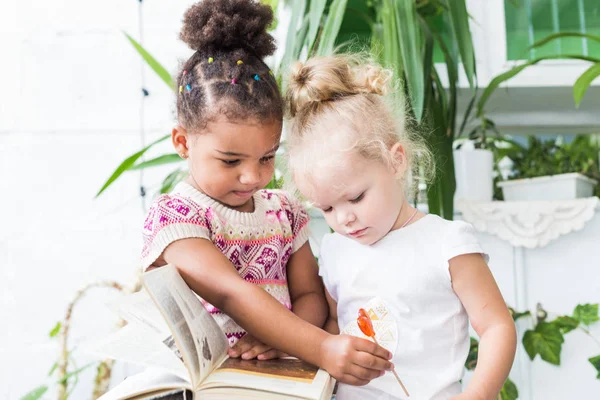 Dua gadis kecil membaca buku tentang latar belakang tanaman dalam pot — Stok Foto