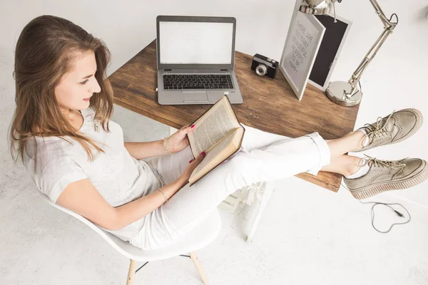 Joven mujer de negocios trabajando en casa y leyendo un libro con las piernas sobre la mesa. Espacio de trabajo de estilo escandinavo creativo. # Wiew from above — Foto de Stock