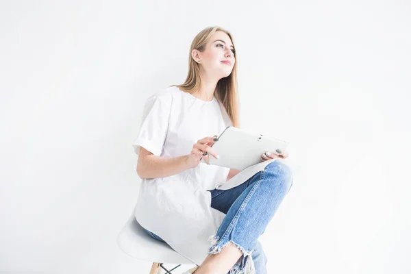 Портрет молодої стильної блондинки в білій футболці і блакитних джинсах, використовуючи планшет на білому тлі — стокове фото