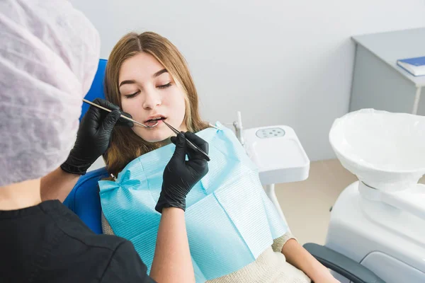 Clínica dental. Recepción, examen del paciente. Cuidado de los dientes. Chica joven se somete a un examen dental por un dentista — Foto de Stock