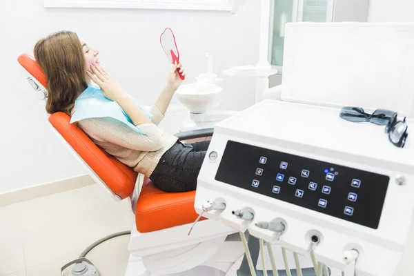 Clínica dentária. Recepção, exame do paciente. Cuidado com os dentes. Menina sorrindo, olhando no espelho depois de um check-up dental em seu dentista — Fotografia de Stock