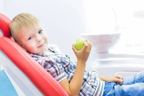 Dental clinic. Reception, examination of the patient. Teeth care. Little boy holding an apple while sitting in a dental chair