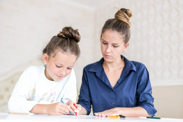 Familia feliz. Madre e hija juntas pintan y dibujan. Mujer adulta ayuda a la niña — Foto de Stock