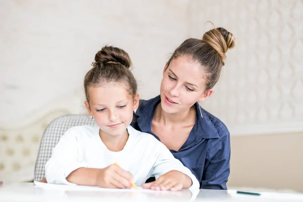 Familia feliz. Madre e hija juntas pintan y dibujan. Mujer adulta ayuda a la niña — Foto de Stock