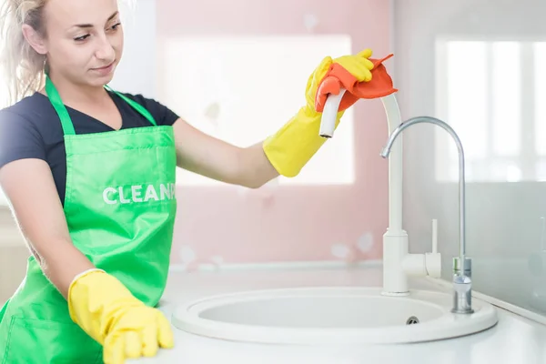 Service de nettoyage. une jeune femme dans un tablier essuie la poussière avec un chiffon — Photo