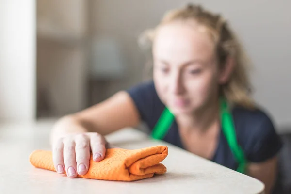Servicio de limpieza. una joven en un delantal limpia el polvo con un trapo — Foto de Stock