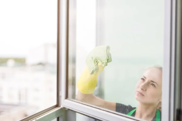 Sonriente joven trabajadora de limpieza jabón suds en ventana de vidrio con escobilla y trapo — Foto de Stock